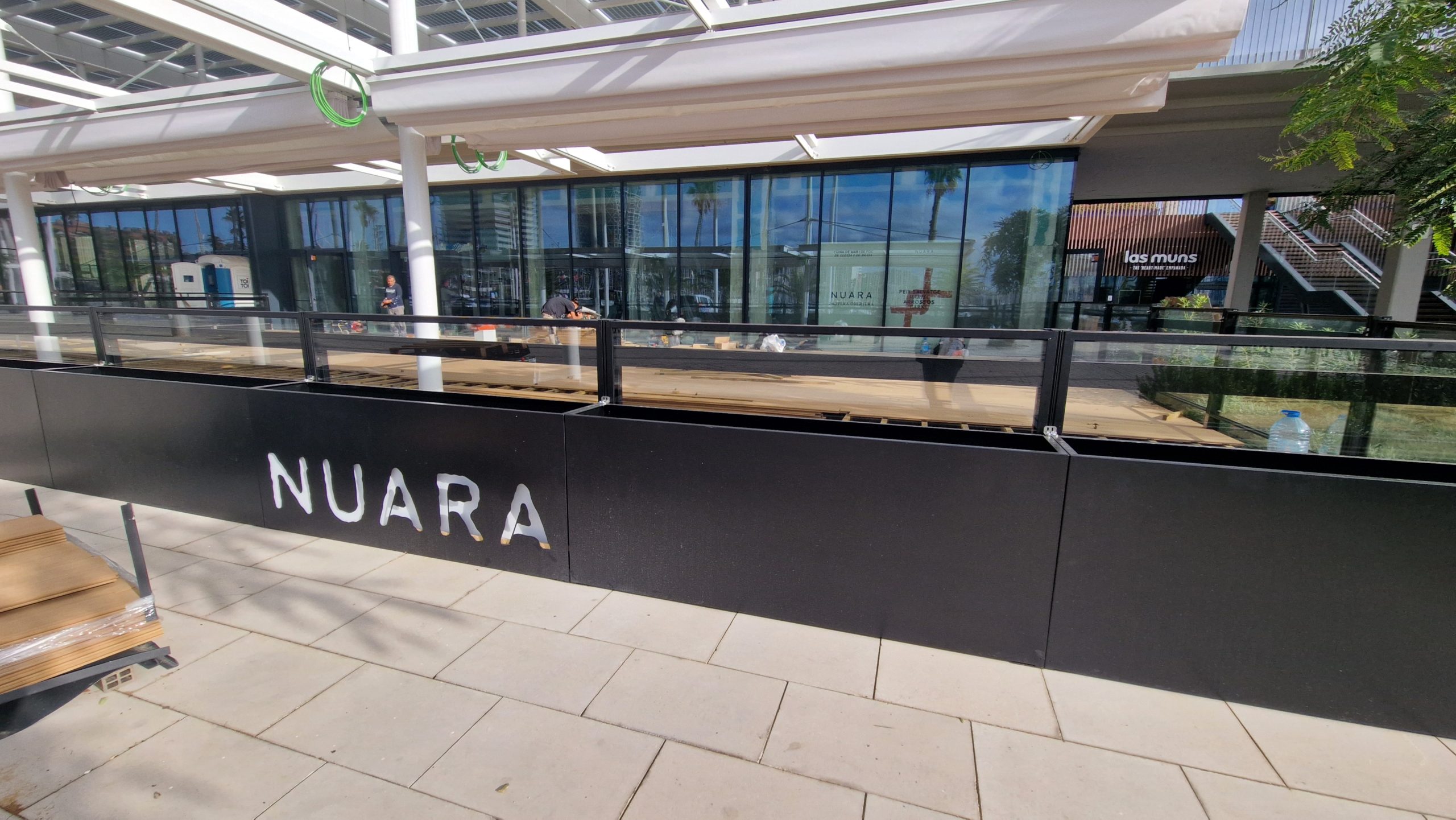 Toldos para terrazas en un espacio abierto con jardineras de color negro y el logo de NUARA
