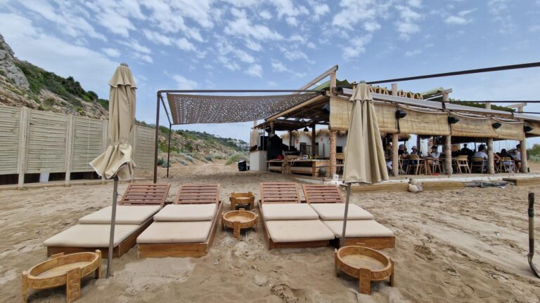 Playa con terraza de un bar, toldo decorativo y tumbonas con sombrillas