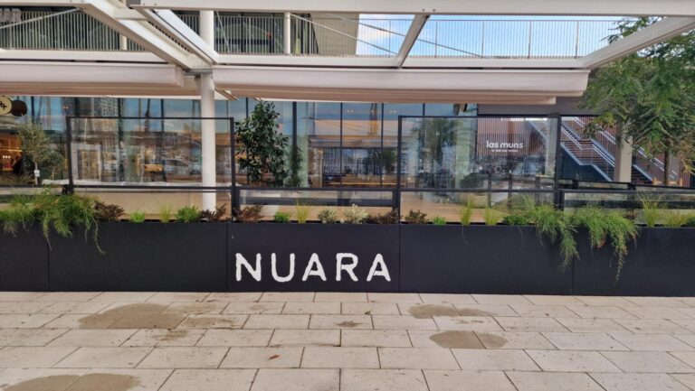 Toldos para terrazas en un espacio abierto con jardineras de color negro y el logo de NUARA
