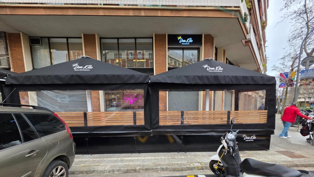 Dos estructuras exteriores contiguas de color negro con toldos y cerramientos laterales transparentes, configurando espacios de terraza para el restaurante Don Kilo.