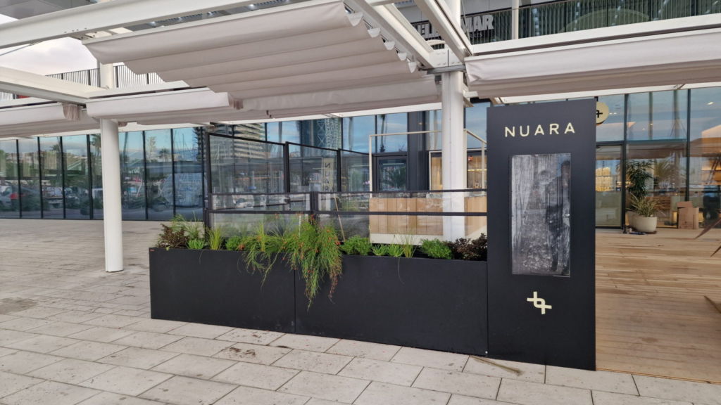 Toldos para terrazas en un espacio abierto con jardineras de color negro y el logo de NUARA