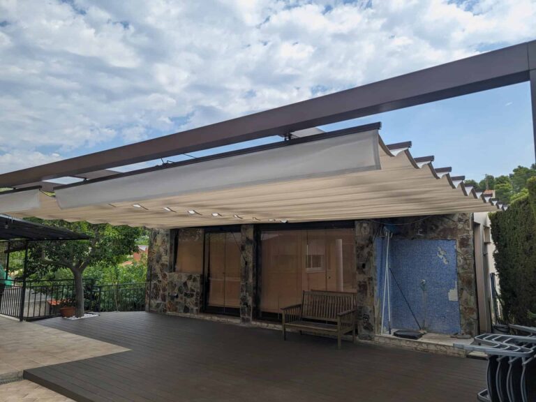 Pérgola de estructura metálica oscura con toldo corredero desplegado sobre terraza con tarima en Viladecavalls.