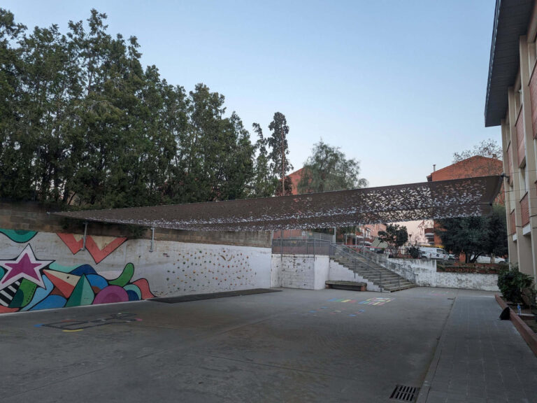 Vela de sombra microperforada sobre la zona de juegos y rocódromo en el patio de la Escola Josep Trueta en Viladecans.