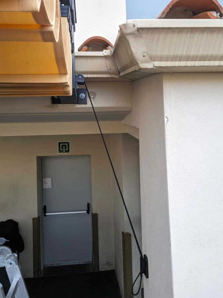 Detalle del anclaje y sistema de polea con cuerda de un toldo corredero plegado en la Escola La Mercè de Martorell.