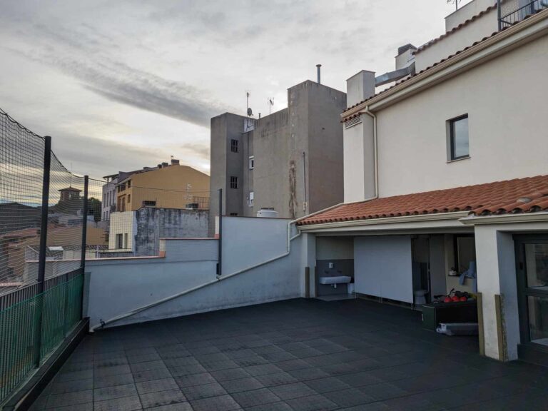 Patio exterior en terraza de la Escola La Mercè en Martorell con pavimento de baldosas y zona cubierta con mamparas divisorias.