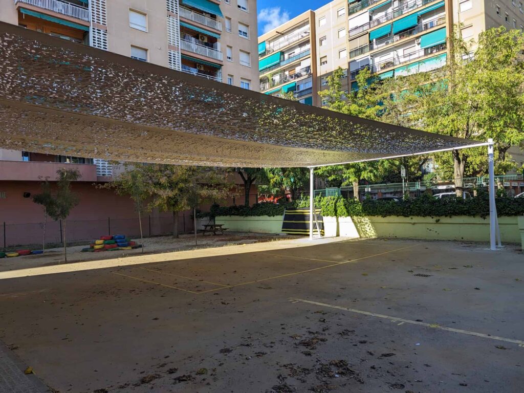 Vela de sombra microperforada instalada sobre postes en el patio de la Escola Les Planes en La Llagosta.