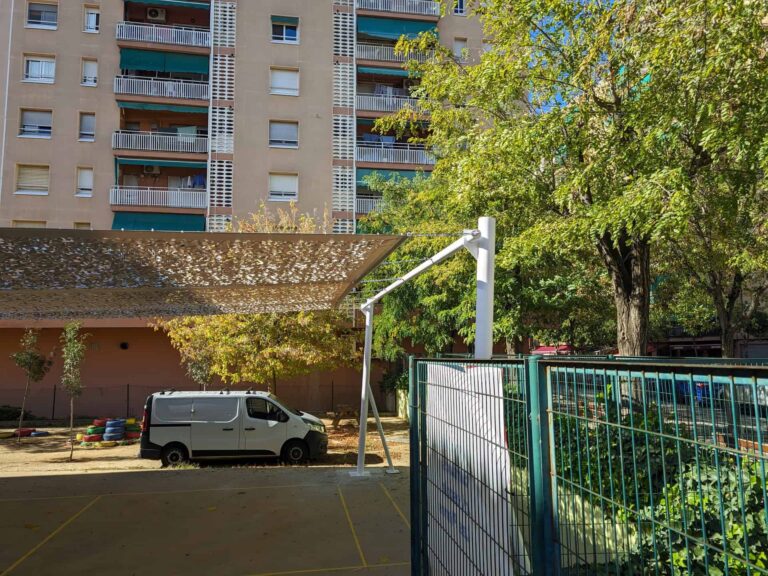 Vela de sombra microperforada fijada a poste metálico blanco en el patio de la Escola Les Planes en La Llagosta.