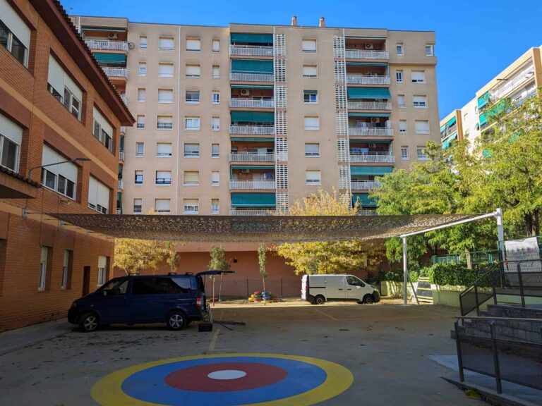Gran estructura de sombra microperforada instalada en el patio de la Escola Les Planes en La Llagosta, fijada a fachada y postes.