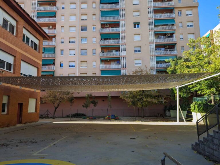 Estructura de vela de sombra instalada en el patio de la Escola Les Planes en La Llagosta, anclada a fachada y poste metálico.