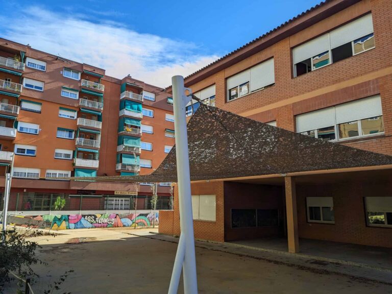 Malla de sombreo tensada fijada a poste blanco y a la fachada del patio escolar de Escola Les Planes en La Llagosta.