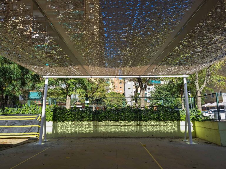 Estructura de sombra con cubierta microperforada sobre postes metálicos en el patio de la Escola Les Planes en La Llagosta.