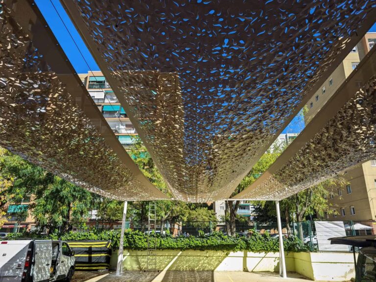 Estructura de sombra con tejido calado sobre postes en el patio de la Escola Les Planes en La Llagosta.