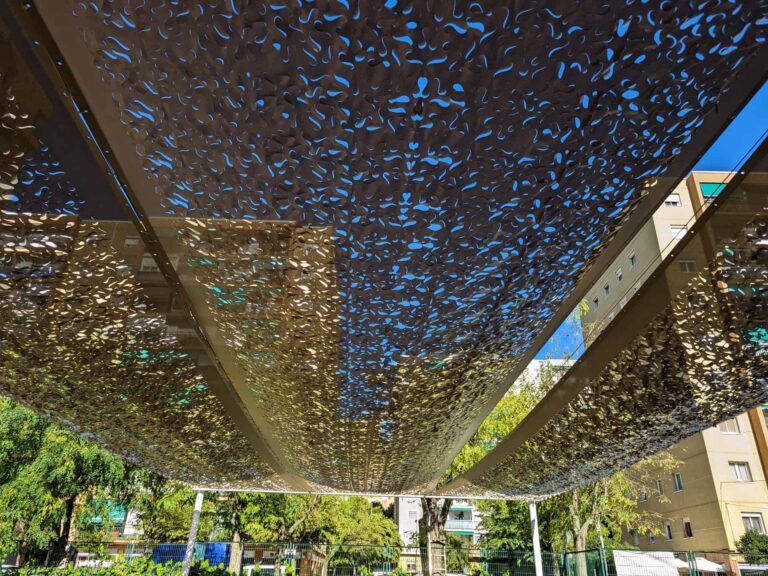 Vista inferior de estructura de sombra con malla calada sobre perfiles metálicos en la Escola Les Planes de La Llagosta.
