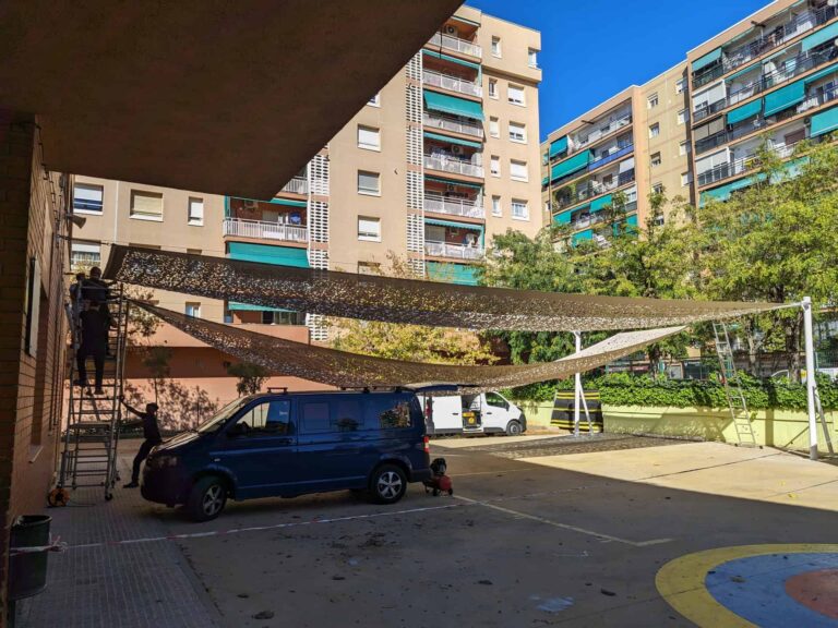 Instalación de velas de sombra caladas en el patio de la Escola Les Planes en La Llagosta, ancladas a fachada y postes.