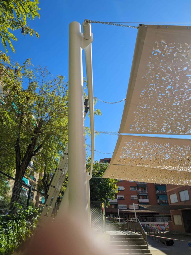 Detalle del poste de anclaje y cadenas de fijación de velas de sombra caladas en el patio de la Escola Les Planes en La Llagosta.
