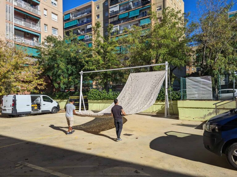 Operarios instalando una tela de sombra en una estructura metálica blanca en el patio de la Escola Les Planes en La Llagosta.