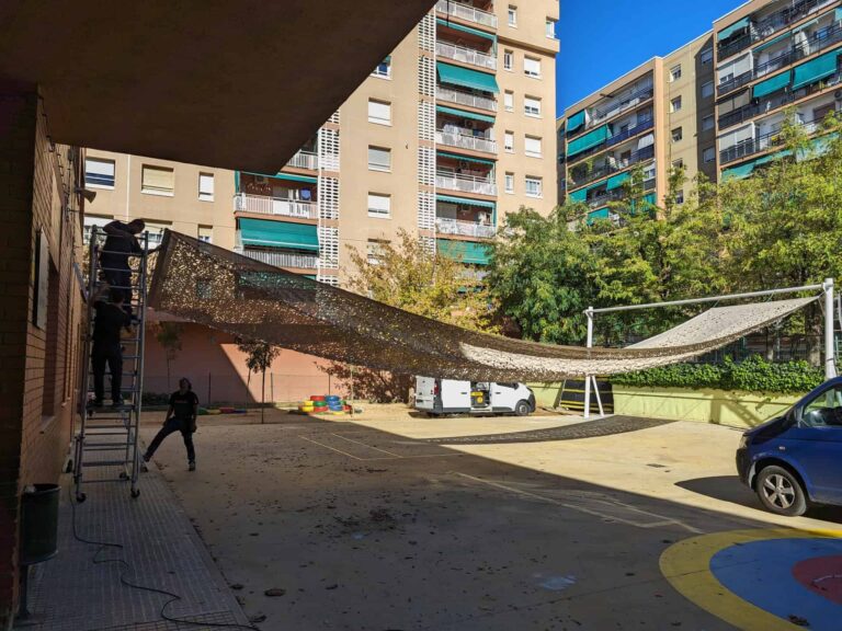 Instalación de malla de sombra en el patio de la Escola Les Planes en La Llagosta mediante anclajes a fachada y postes.