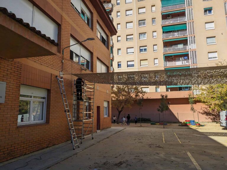 Instalación de malla de sombra calada anclada a la fachada de ladrillo en el patio de la Escola Les Planes en La Llagosta.