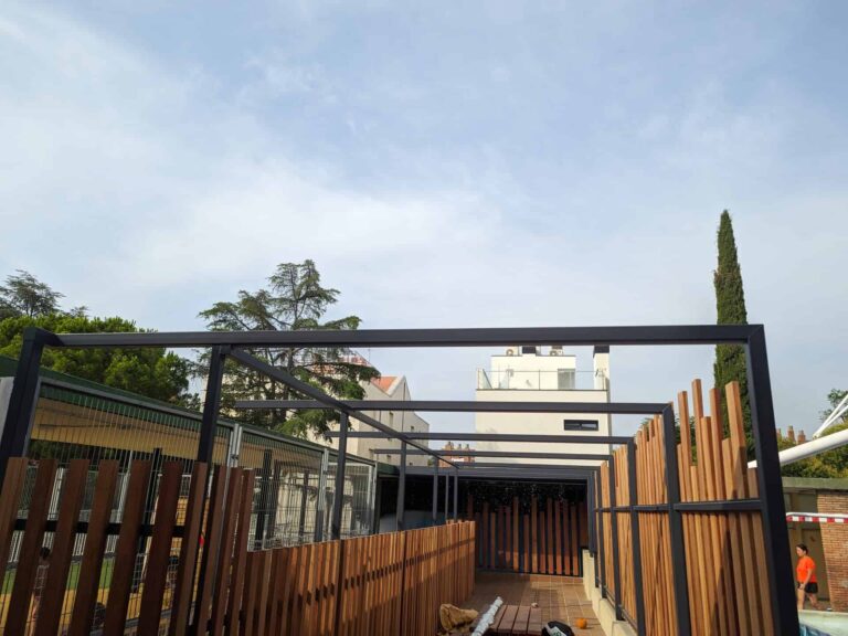Estructura de pérgola metálica con cerramiento de listones de madera en pasillo exterior de la Escola Regina Carmeli en Horta.