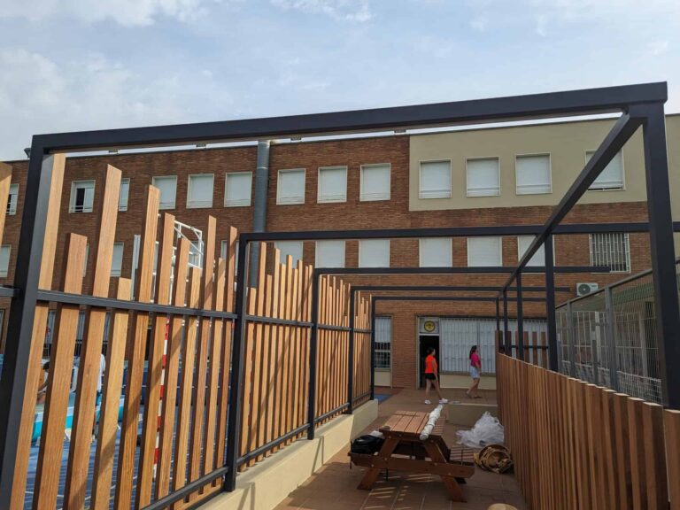 Estructura de pérgola metálica con cerramiento de lamas de madera en el patio de la Escola Regina Carmeli en Horta.