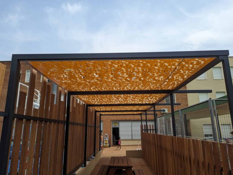 Pérgola con cubierta calada de sombraje y laterales de listones de madera en el patio de Escola Regina Carmeli en Horta.