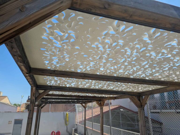 Pérgola de madera con cubierta textil calada de sombreo instalada en el patio exterior de la Escola Ribatallada en Sabadell.
