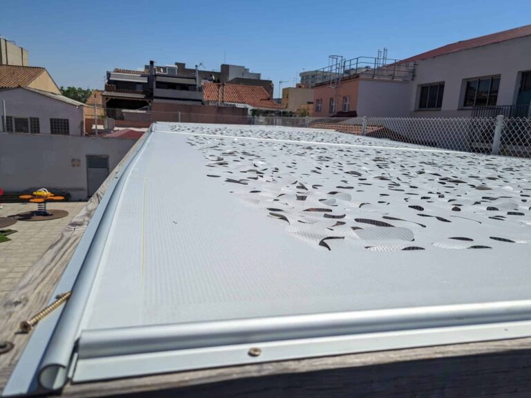 Vista superior de cubierta de sombra con tejido calado sobre estructura de madera en la Escola Ribatallada de Sabadell.