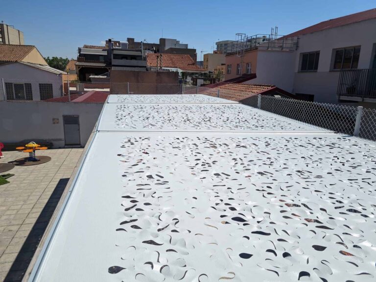 Vista superior de estructura de sombra con paneles perforados blancos en el patio de la Escola Ribatallada en Sabadell.