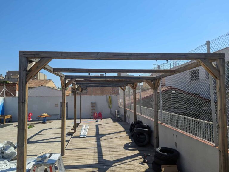 Montaje de estructura de pérgola de madera sobre tarima exterior en el patio de la Escola Ribatallada en Sabadell.
