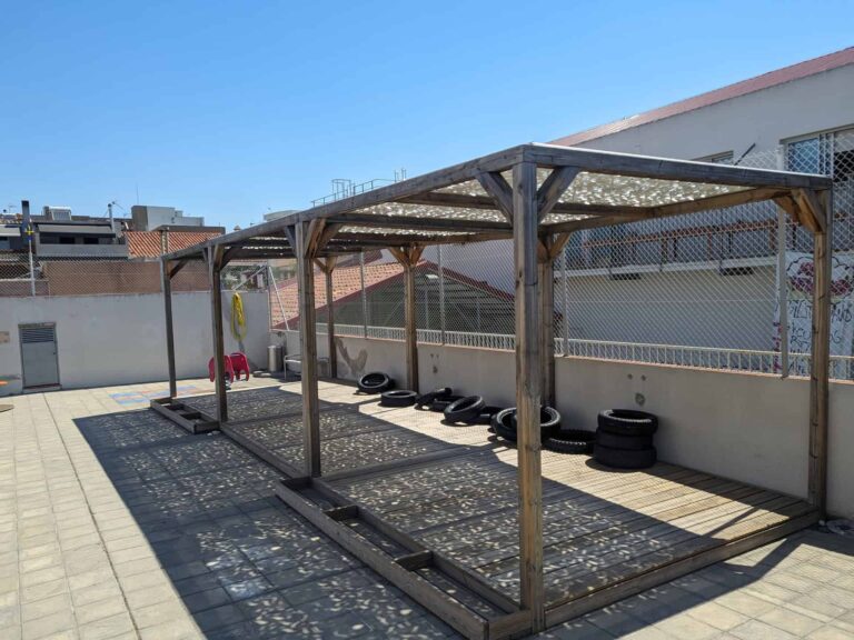 Pérgola de madera con cubierta microperforada y tarima en el patio de la Escola Ribatallada en Sabadell.
