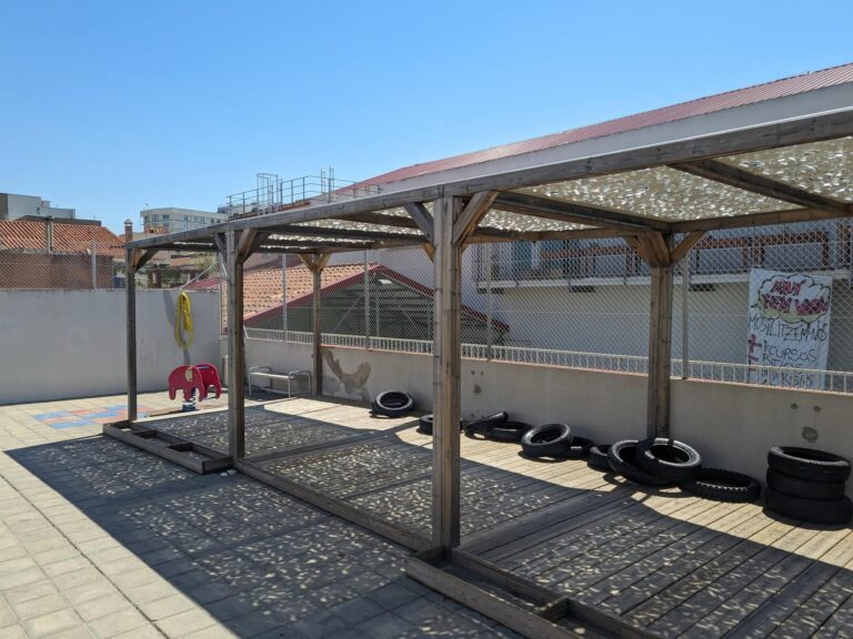 Pérgola de madera con tarima y cubierta microperforada de sombra instalada en el patio de la Escola Ribatallada en Sabadell.