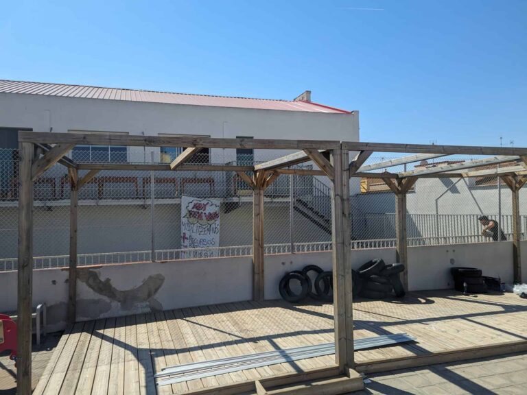 Estructura de pérgola de madera instalada sobre tarima en el patio exterior de la Escola Ribatallada en Sabadell.