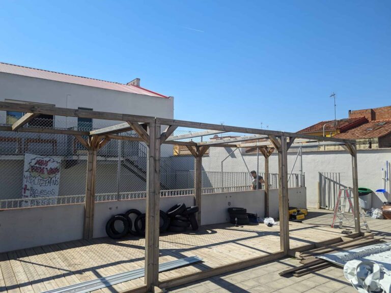 Montaje de estructura de pérgola de madera sobre tarima en el patio de la Escola Ribatallada en Sabadell.