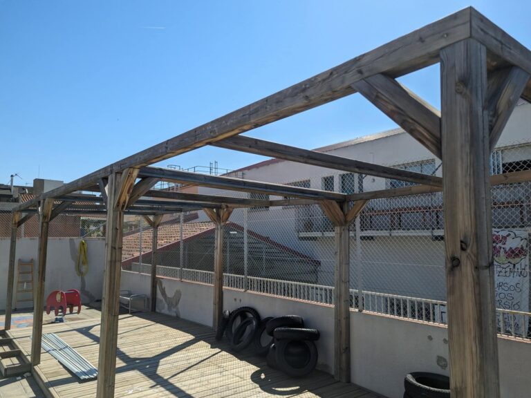 Estructura de pérgola de madera instalada sobre tarima exterior en el patio de la Escola Ribatallada en Sabadell.