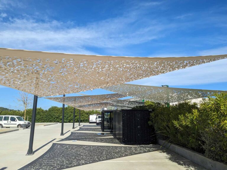 Velas tensadas microperforadas en tonos claros sobre postes metálicos en el exterior del Hotel Ona Brava en Santa Susanna.