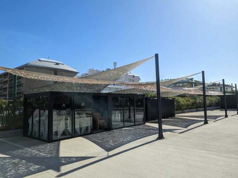 Velas tensadas caladas fijadas a postes metálicos sobre terraza exterior y módulo acristalado en Hotel Ona Brava, Santa Susanna.