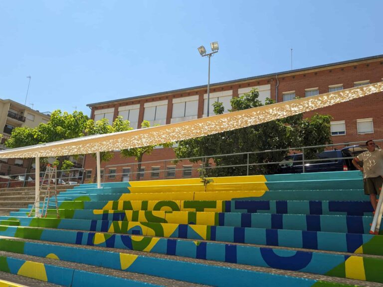 Instalación de estructura de sombra con malla calada sobre gradas exteriores pintadas en el Institut El Cairat de Esparreguera.