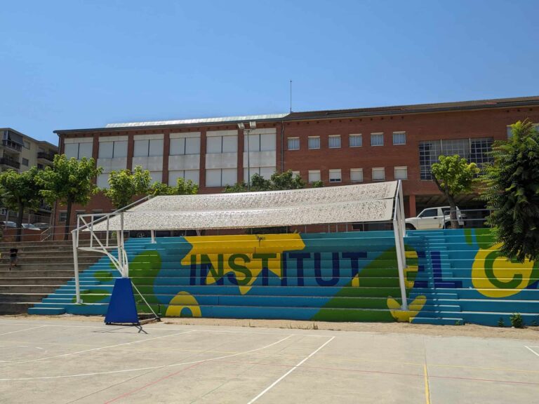 Estructura de sombra metálica instalada sobre las gradas pintadas del patio del Institut El Cairat en Esparreguera.