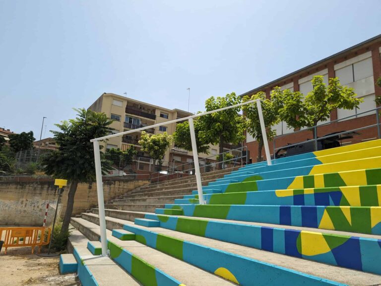 Estructura metálica blanca instalada sobre gradas pintadas en el patio del Institut El Cairat en Esparreguera.