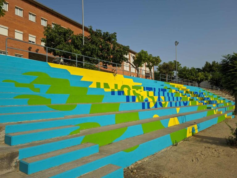 Gradas exteriores de hormigón con mural gráfico pintado en el patio del Institut El Cairat en Esparreguera.