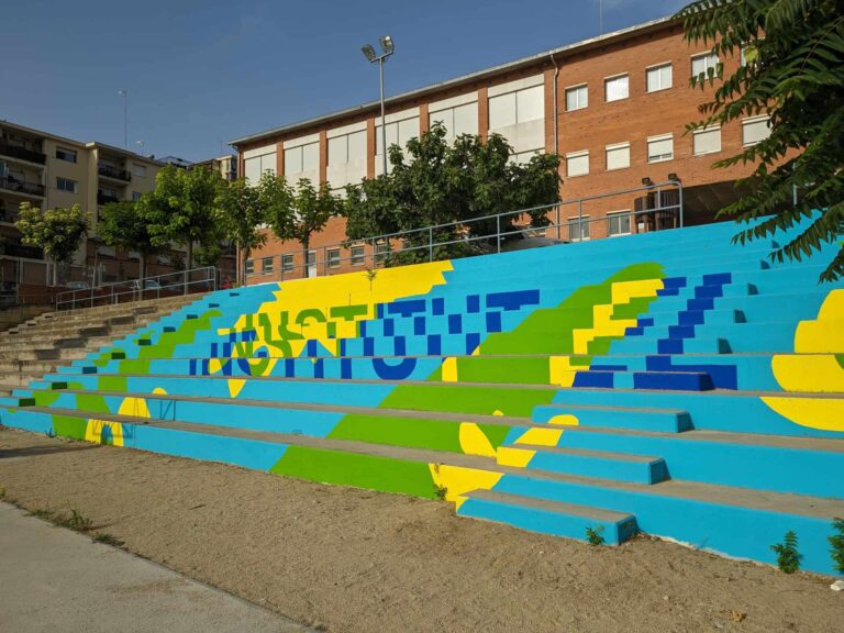 Gradas exteriores pintadas de colores vivos en el patio del Institut El Cairat en Esparreguera, frente al edificio escolar.