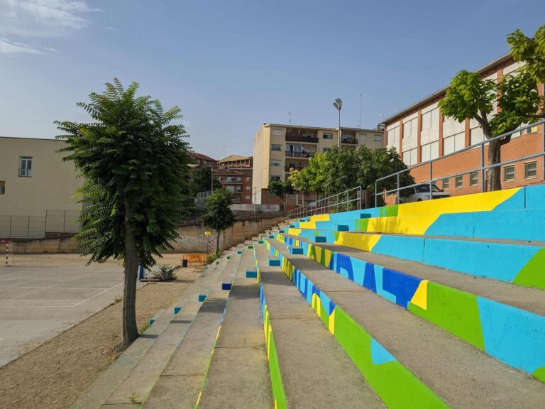 Gradas escalonadas pintadas de colores junto a la pista deportiva en el patio del Institut El Cairat en Esparreguera.