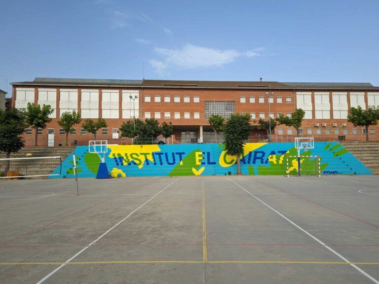 Pista polideportiva exterior y fachada del Institut El Cairat en Esparreguera con gradas y mural pintado.