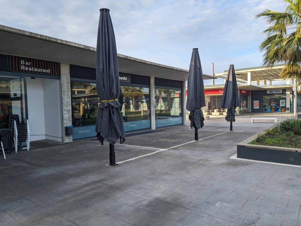 Parasoles de gran tamaño plegados y anclados en el suelo de la terraza exterior del restaurante Koi Sushi en Port Premià.