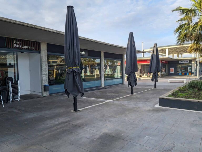 Parasoles de gran tamaño plegados y anclados en el suelo de la terraza exterior del restaurante Koi Sushi en Port Premià.