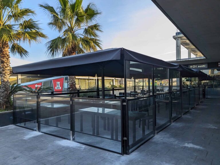 Terraza exterior con cerramiento de mamparas transparentes y grandes parasoles oscuros en Koi Sushi Port Premià.