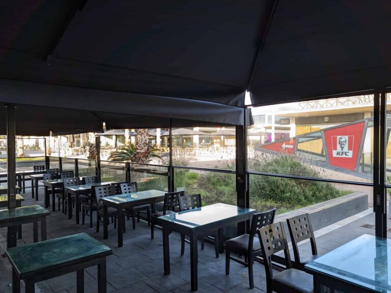 Terraza de restaurante con cerramiento perimetral de vidrio, cubierta oscura y mesas dispuestas en Port Premià.