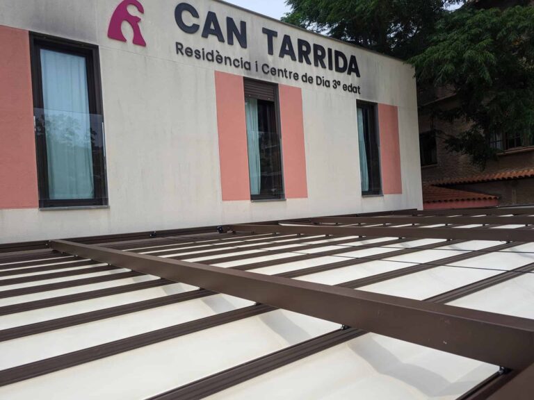 Vista superior de pérgola con cubierta textil retráctil y perfiles oscuros junto a la fachada de Can Tarrida en Torrelles de Llobregat.